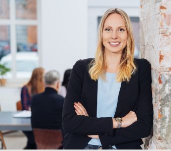 BerufsWege für Frauen und Social Business Women e.V., Weiterbildung für Frauen, Frau lehnt selbstbewusst an einer Wand, in einem hellem und modernen Büro