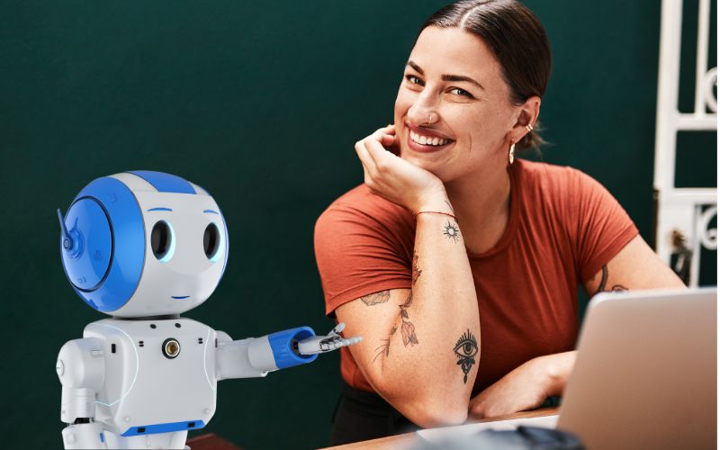 WS Videos und Audios mit KI_Weiterbildung BerufsWege für Frauen e. V., eine Frau arbeitet am Laptop, animierter Bot unterstützt sie