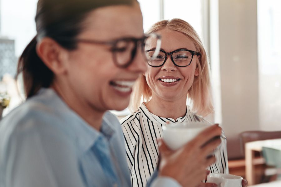 Zwei Frauen stehen im Büro, trinken Kaffee zusammen und lachen, BeufsWege für Frauen e. V., Weiterbildung für Frauen
